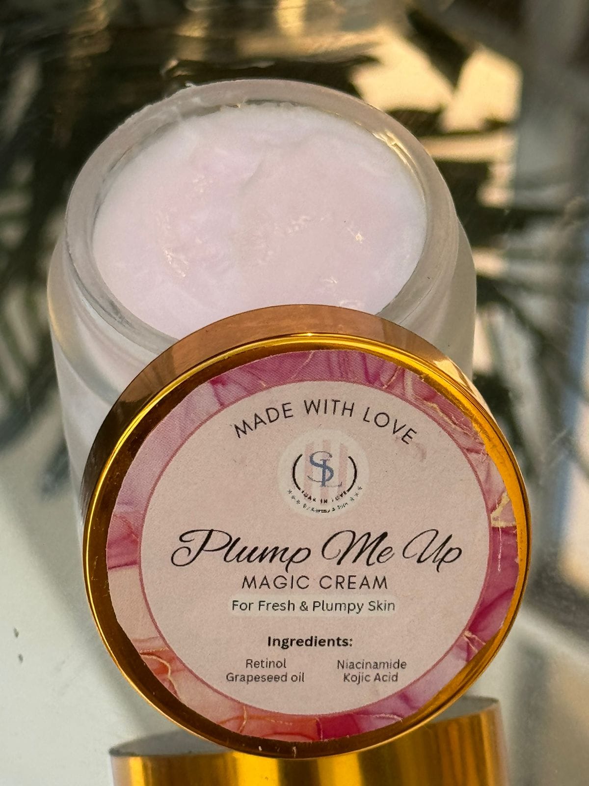 An open jar of Soak in Love's Plump Me Up (Magic Cream) displays the nourishing cream inside. The label states "Made with Love" and highlights natural ingredients like retinol, grapeseed oil, niacinamide, and kojic acid. This product guarantees revitalized, plump skin with a radiant glow.